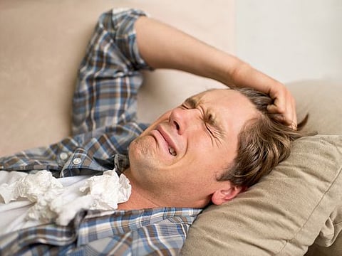 A young man crying while lying on the sofa with tissues.