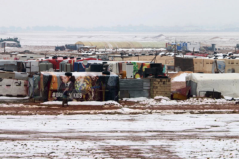 A Syrian refugee walks past makeshift shelters 091
