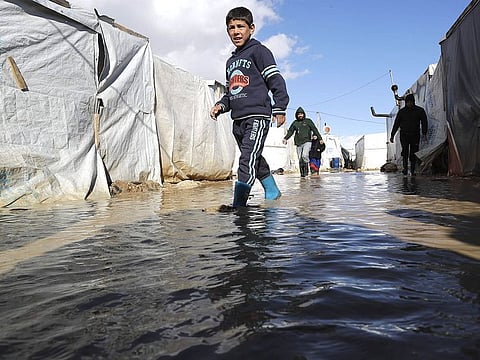 A child wades through rain and snow waters at an informal tent settlement housing Syrian refugees following winter storms in the area of Delhamiyeh, in the central Bekaa Valley