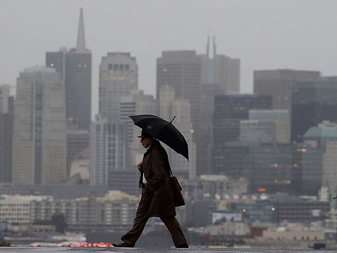 A man carries an umbrella as he crosses the street with the skyline at rear in San Francisco, Friday, Feb. 1, 2019. 