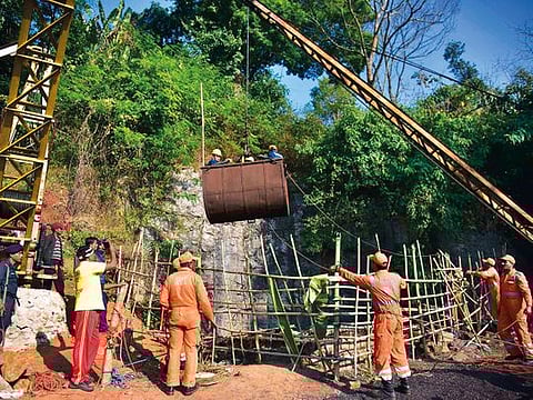 National Disaster Response Force (NDRF) personnel gather around a crane while Indian Navy divers are lifted with a pulley