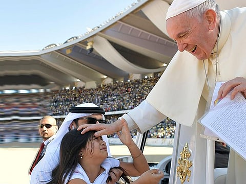The girl in white shirt and pink pants went under the railings and ran to the Pope to deliver a card.