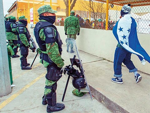 A man wrapped in a Honduran flag passes a cordon of military police outside a shelter for migrants in Piedras Negras, Mexico, near the US border, where about 1,700 migrants travelling by caravan reached the US-Mexican border on Sunday.
