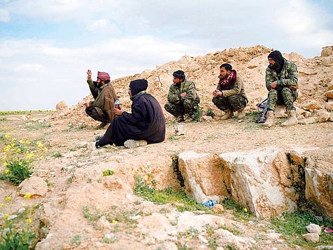 U.S.-backed Syrian Democratic Forces (SDF) fighters sit atop a hill in the desert outside the village of Baghouz, Syria