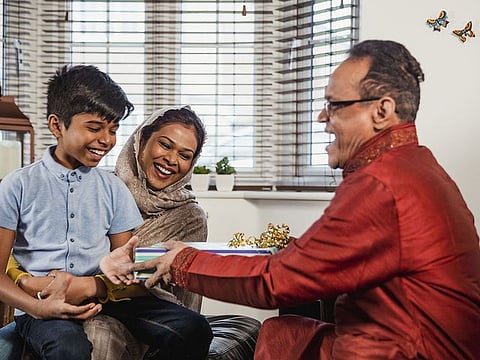 A senior man wearing a kurta gives a gift to his grandson.