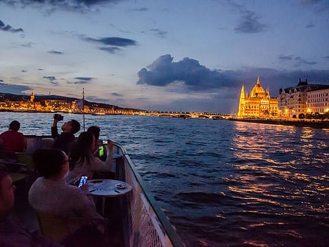 People on boat aver Danube river taking picture during summer night ride