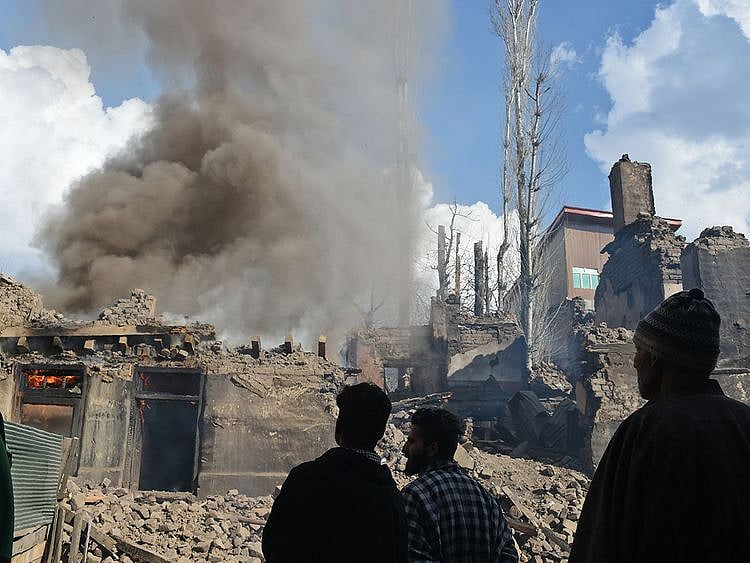 Kashmiri villagers look on a fire razes
