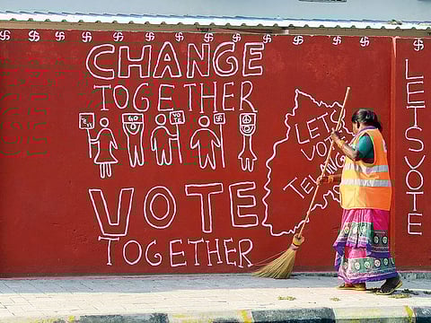 Indian sweeper cleans a footpath as a graffiti reading "change together vote together" is written on the wall in Hyderabad.