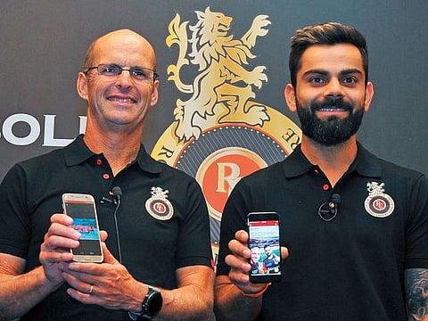 RCB team coach Gary Kristen and skipper Virat Kohli display the RCB mobile application during its launch in Bengaluru
