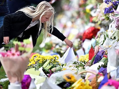 A young girl places a note among flowers left in tribute to victims in Christchurch