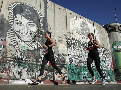 Athletes run past a mural depicting the Palestinian Leila Khaled, the 1970 Popular Front for the Liberation of Palestine (PFLP) El Al aircraft hijacker, drawn along Israel's controversial separation barrier in the biblical town of Bethlehem in the occupied West Bank during the 7th International Palestine Marathon on March 22, 2019.
