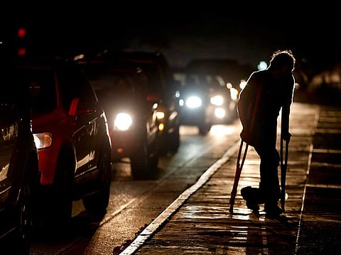 In this March 29, 2019 file photo, a man on crutches is illuminated by headlights of oncoming traffic, in Caracas, Venezuela.