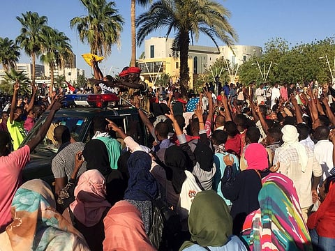 Sudanese demonstrators flash the victory sign as a military police vehicle drives past them during a protest demanding Sudanese President Omar Al-Bashir to step down in Khartoum