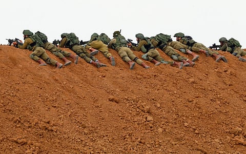 In this file photo taken on March 30, 2018 Israeli soldiers keep position as they lie prone over an earth barrier along the border with the Gaza Strip in the southern Israeli kibbutz of Nahal Oz as Palestinians demonstrate on the other side commemorating Land Day.