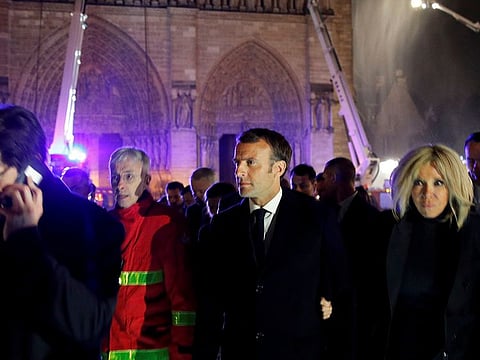 French President Emmanuel Macron, center, and his wife Brigitte walk away from Notre Dame cathedral in Paris, Monday, April 15, 2019.