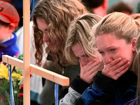 In this April 22, 1999, file photo, Columbine High School students, from left, Darcy Craig, Molly Byrne and Emily Dubin stop to pay their respects at a makeshift memorial set up in a park near the high school in Littleton, Colorado.