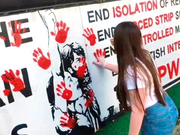 A number of women smear red paint in hand prints
