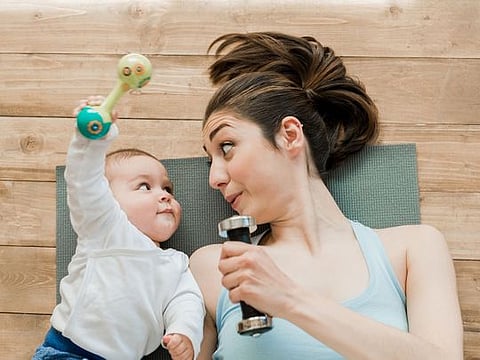 A mother with baby boy lying on floor and playing with dumbbells