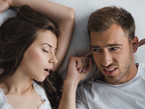 Husband closing ears and looking at snoring wife (Illustrative purposes only) 