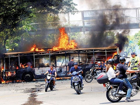 People drive their motorcycles near a burnt bus during antigovernment protests, in Caracas on Tuesday. 