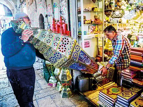 Palestinian craftsman Essam Zughair helps an elderly man carry a large Ramadan lantern in his shop in the old city of occupied Jerusalem.