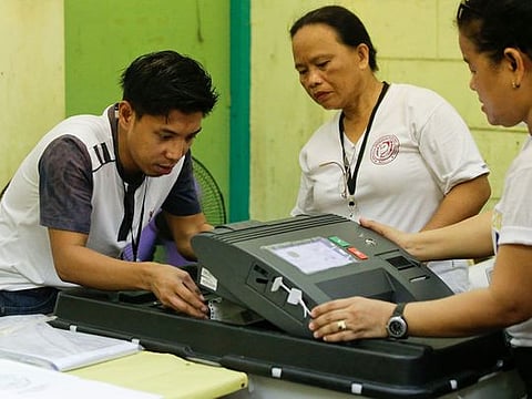 Election workers try to fix a jammed ballot inside a counting machine at a polling center in the Manuel L. Quezon elementary school, Manila, Philippines.