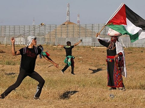 A protester hurls stones at Israeli troops as a woman wearing a traditional Palestinian outfit waves a national flag, during a demonstration near the border with Israel, east of Gaza City, on May 10, 2019.
