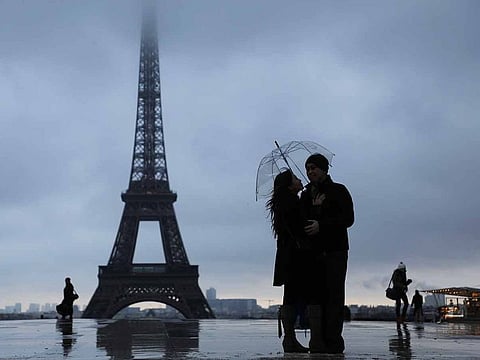 A couple standing under an umbrella to shelter from the rain and snow on the Trocadero Plaza with the Eiffel Tower in the background in Paris. 