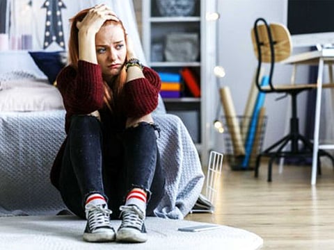 Worried, young girl holding her head, witting on the floor in her bedroom