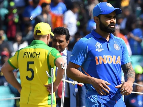 Indian skipper Virat Kohli (right) walks on the field as Australia's captain Aaron Finch (L) is interviewed ahead of the start of their World Cup group stage match at The Oval in London on June 9, 2019. 