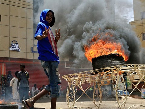 A Sudanese protester gestures as he walks past burning tyre near Khartoum's army headquarters on June 3, 201 9 after security forces broke upa weeks-long sit-in. 