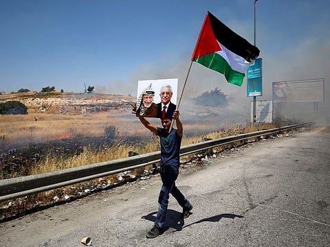 A demonstrator holds a Palestinian flag and a picture of late Palestinian leader Yasser Arafat and President Mahmoud Abbas during a protest against Bahrain's workshop for U.S. peace plan, near the Jewish colony of Beit El, in the Israeli-occupied West Bank June 24, 2019.