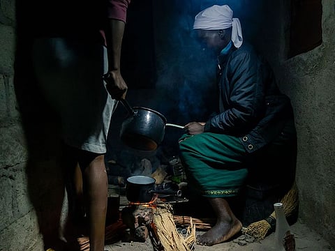Egenia Chishapira sits close by an open fire lit with a torch light as she uses firewood to prepare an evening meal for her family at her home in Mbare township, Harare, on June 21, 2019. 
