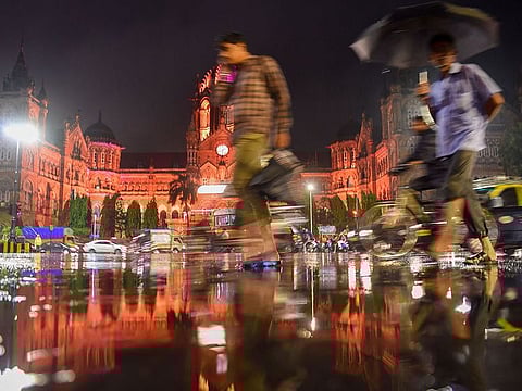 People pass in front of Chhatrapati Shivaji Terminus as it rains  in Mumbai.