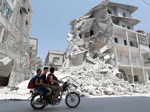 A Syrian man drives a motorcycle past destroyed buildings in the town of Ariha, in the south of Syria's Idlib province, on August 2, 2019.