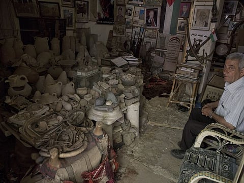 Walid al-Aqqad sits next to Palestinian heritage pieces and antiques piled up inside his private museum in town of Khan Younis, Southern Gaza Strip.