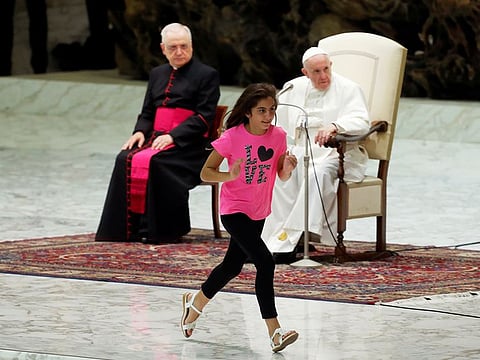 A girl runs next to Pope Francis as he leads the weekly general audience in Paul VI Hall at the Vatican.