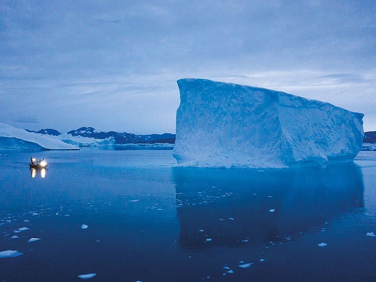 A boat navigates at night next to large icebergs in eastern Greenland. 