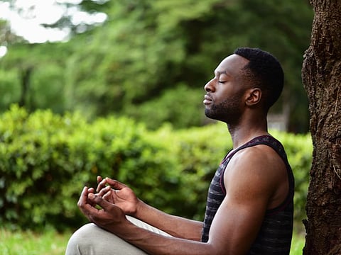 A young man sitting on the ground at a park, meditating.