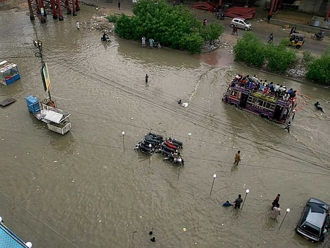 An overloaded bus drives through a flooded road caused by heavy monsoon rains, in Karach