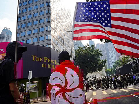 A protester wraps himself with Hong Kong flag, with the U.S. flag seen at right, as they march from Chater Garden to the U.S. Consulate in Hong Kong