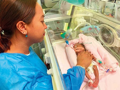 Louie with daughter Faith in a neonatal crib in the hospital. The family is currently facing hospital expenses of Dh4,000 a day.
