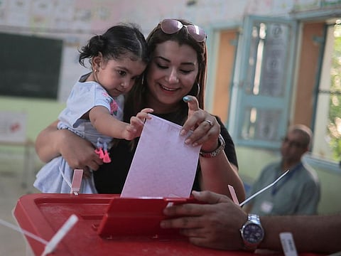 A voter casts her ballot as she carries her daughter inside a polling station