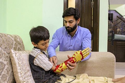 WPK 2. Bioniks CTO and robotics engineer Anas Niaz fixing the bionic arm as little Bilal eagerly waits to use his Iron Man arm. Photo taken at Bilal's home in Rawalpindi. Image Credit - Sana Jamal_Gulf News-1570190982443