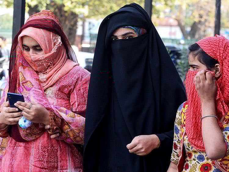 Women look on as they use mobiles phones in Srinagar