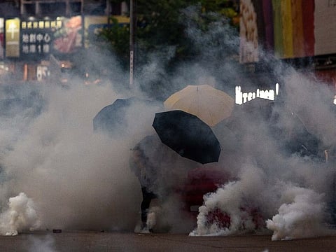 Demonstrators hold umbrellas while shrouded by tear gas during a protest in the Mong Kok district of Hong Kong, China, on Sunday, Oct. 20, 2019.