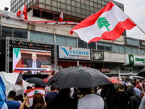 Lebanese people take cover from the rain under umbrellas as they watch a televised speech by President Michel Aoun, during a demonstration on the eighth day of protest against tax increases and official corruption, in Zouk Mosbeh, north of the capital Beirut, on October 24, 2019. 