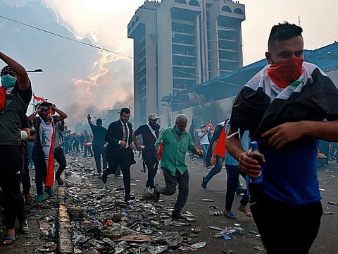 Anti-government protesters run to take cover while Iraqi Security forces fire tear gas during a demonstration