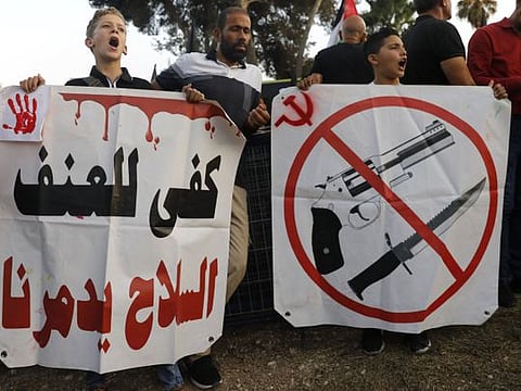 Palestinian citizens of Israel carry a placard reading in Arabic, "enough with violence, arms are destroying us" as they protest outside the district police headquarters in the Arab Israeli city of Nazareth during a demonstration against violence, organised crime and recent killings among their communities, on October 22, 2019.  