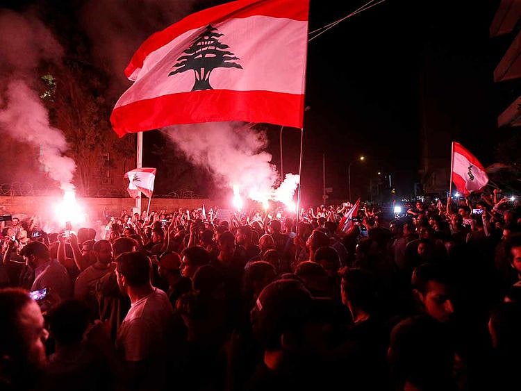 Demonstrators hold flares and Lebanese flags as they protest outside the house of former Lebanese prime minister Fouad Siniora in Beirut